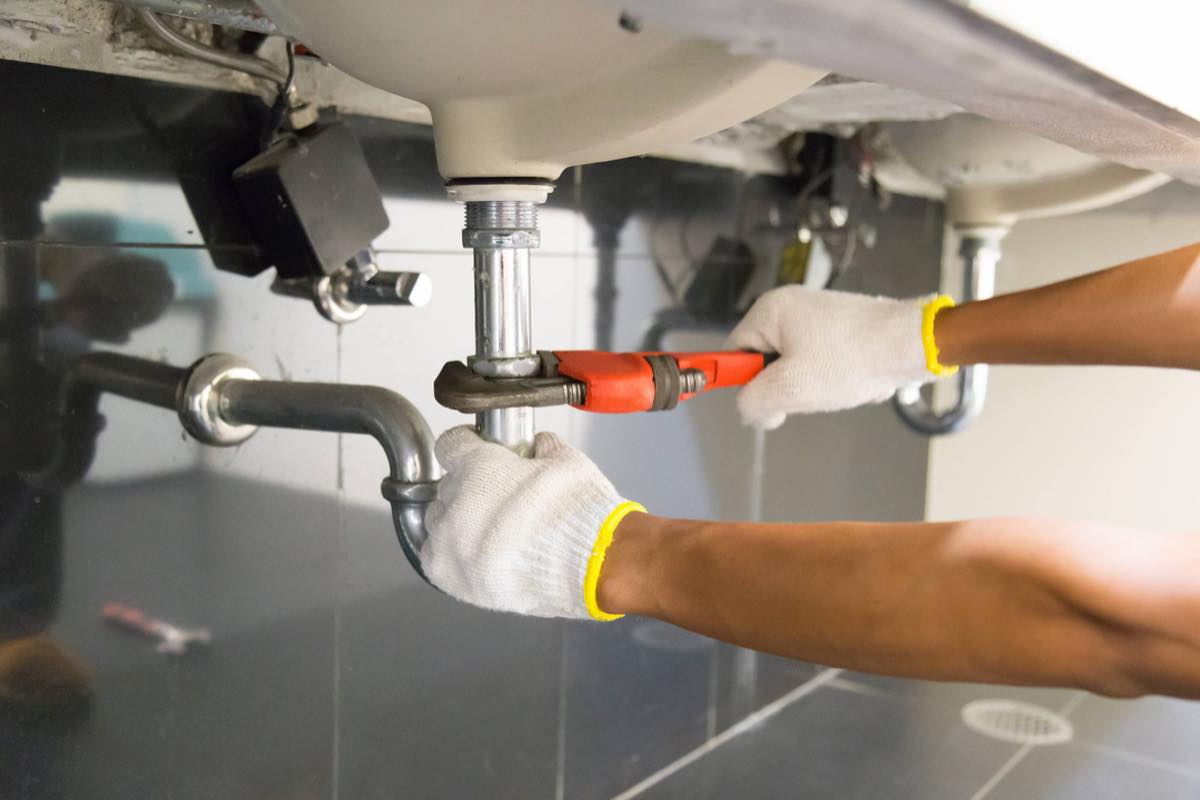 Plumber fitting a new trap and waste pipe beneath a basin